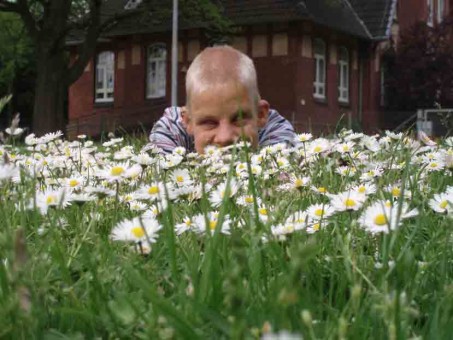 Ein Internatsschüler liegt auf einer Blumenwiese. Im Hintergrund sieht man die Wohngebäude der Internate.