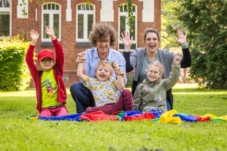 Drei Vorschulkinder mit zwei Lehrkräften auf der Wiese