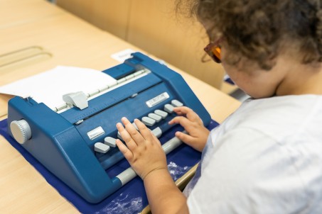 Blick über die Schulter einer Schülerin, welche an einer Punktschriftmaschine arbeitet.