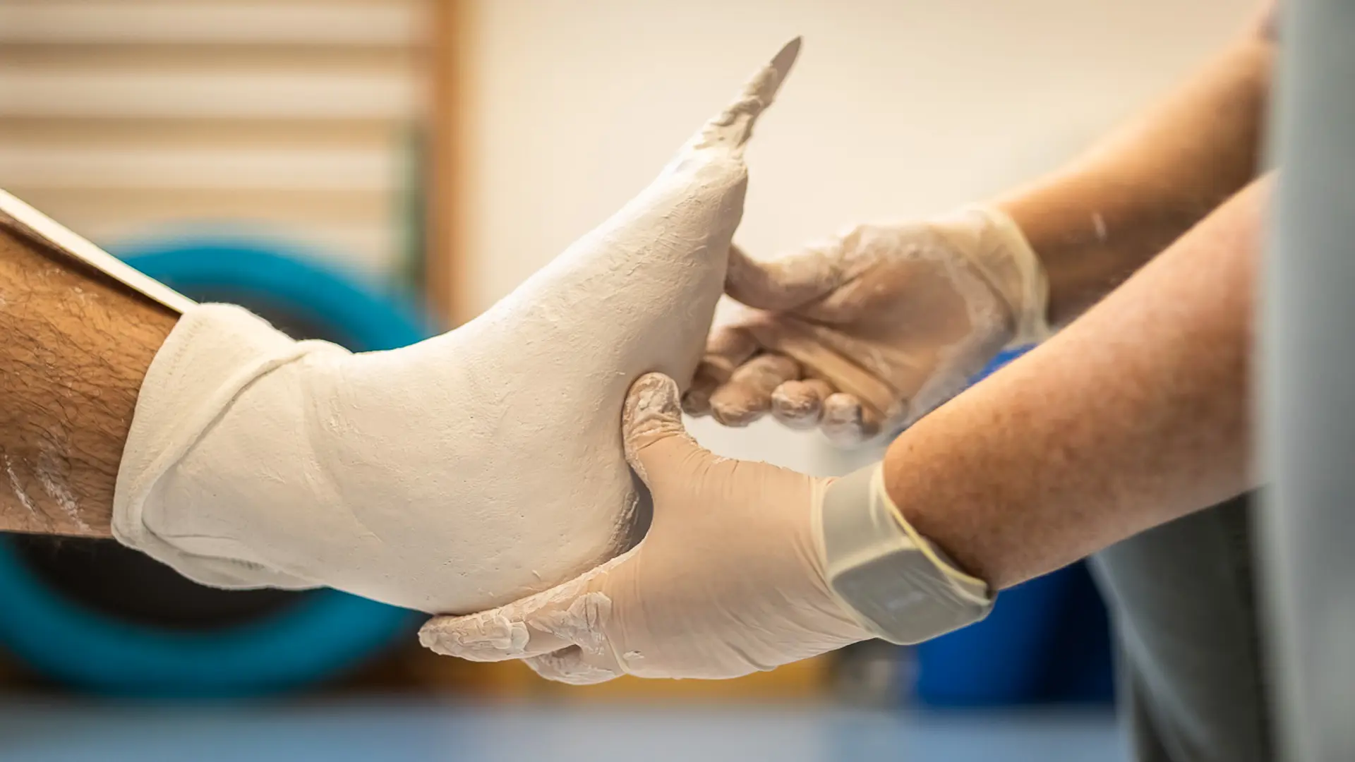 Auf dem Bild ist ein Fuss mit Gips zu sehen, der von den Händen eines Arztes gehalten und untersucht wird.