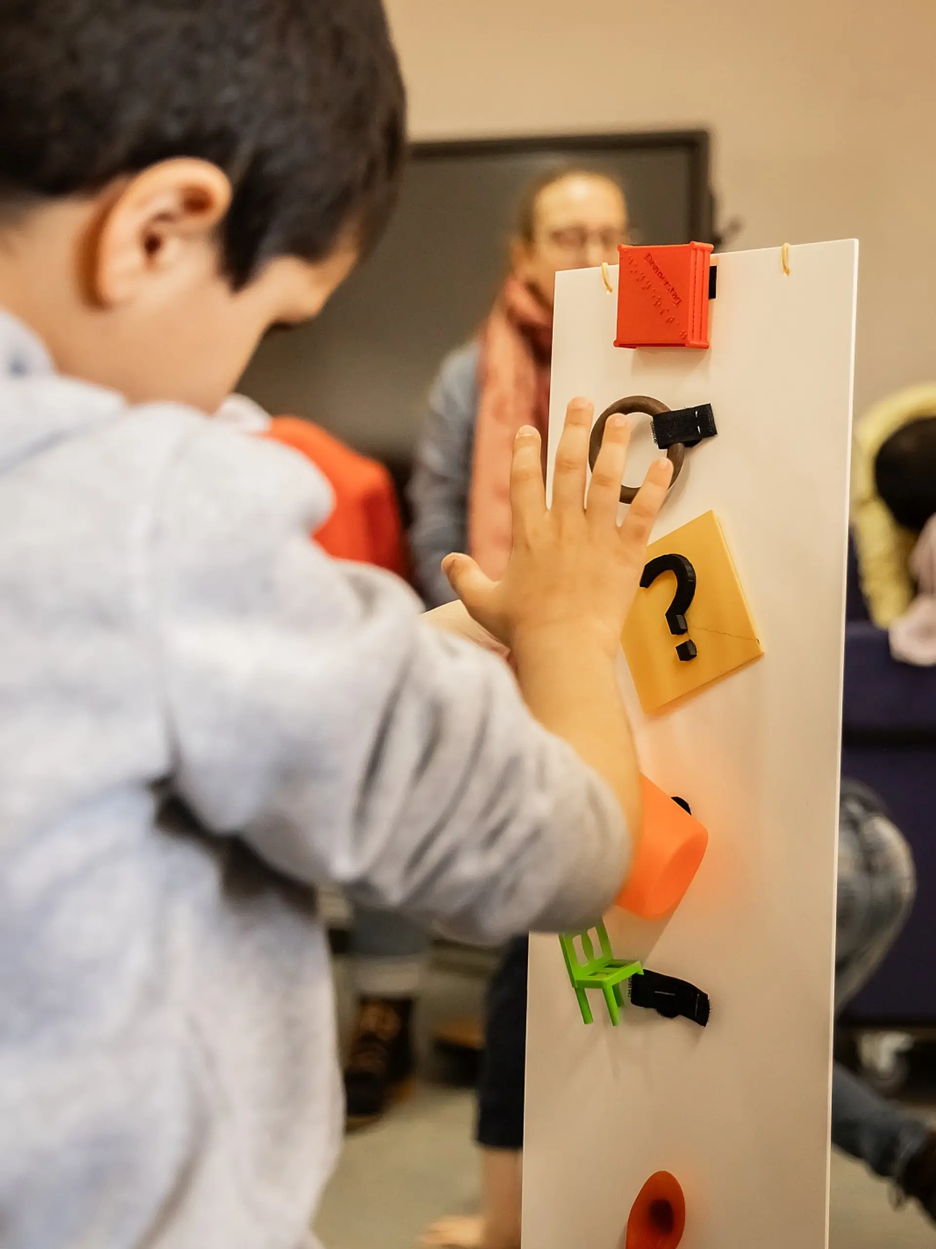 Ein Schüler steht vor einer Leiste, die ungefähr so hoch ist wie er. Er ertastet die handgroßen Objekte, die extra darauf befestigt sind, damit er ihre Form kennenlernt.