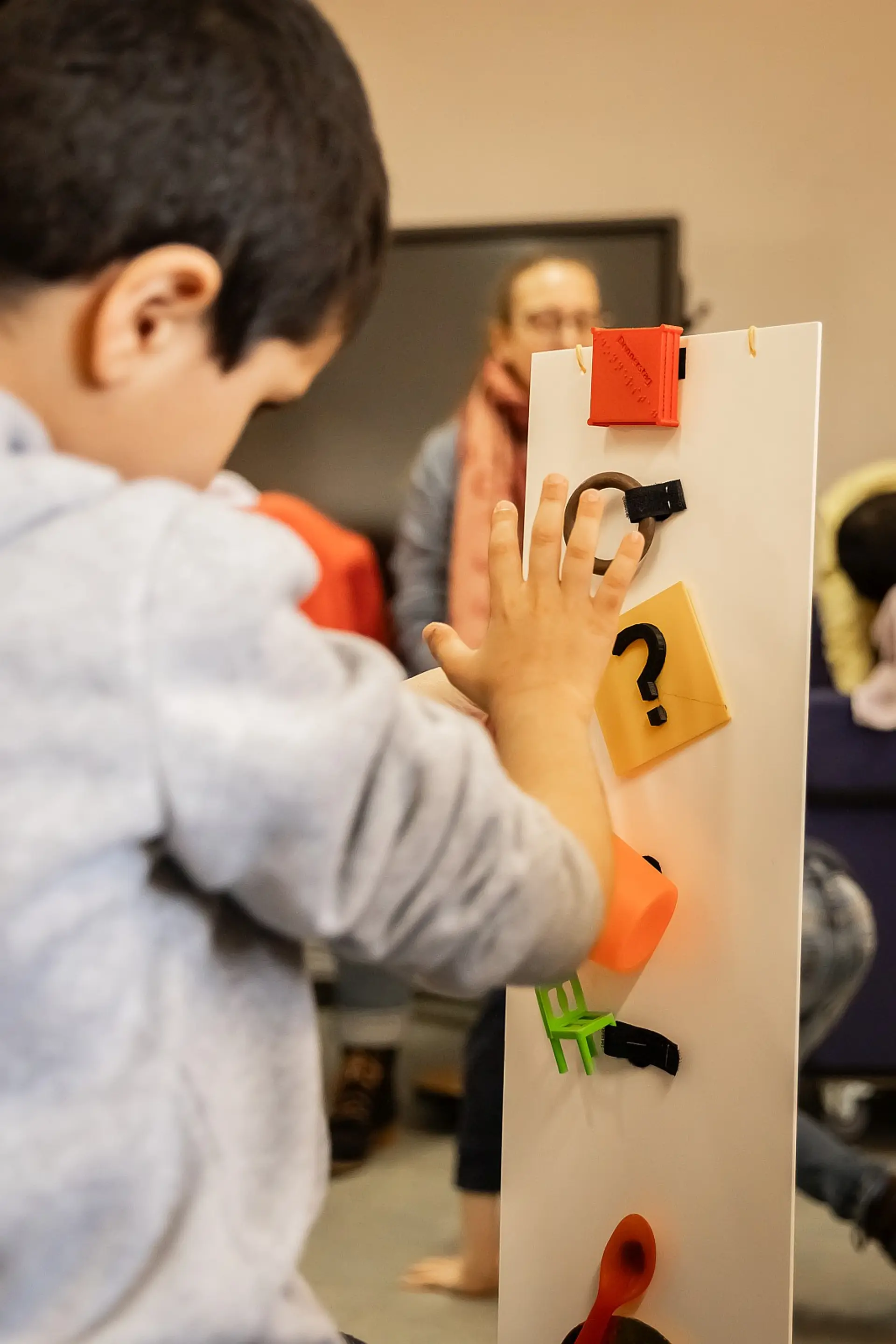 Ein Schüler steht vor einer Leiste, die ungefähr so hoch ist wie er. Er ertastet die handgroßen Objekte, die extra darauf befestigt sind, damit er ihre Form kennenlernt.