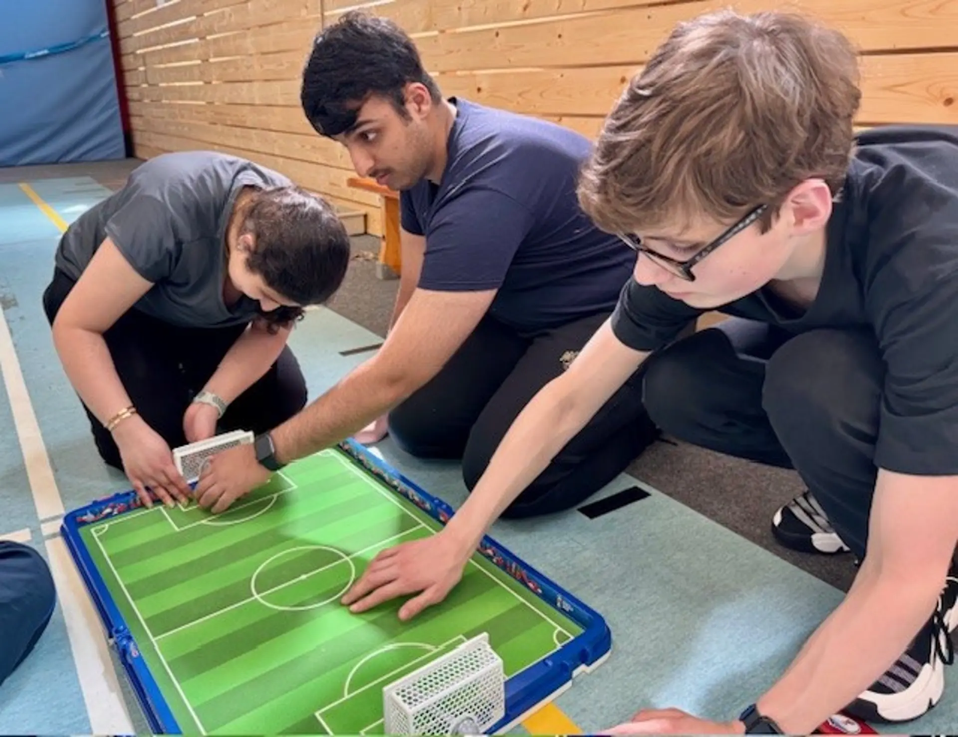 Drei Schüler*innen erkunden ein Modell eines Fußballplatzes.