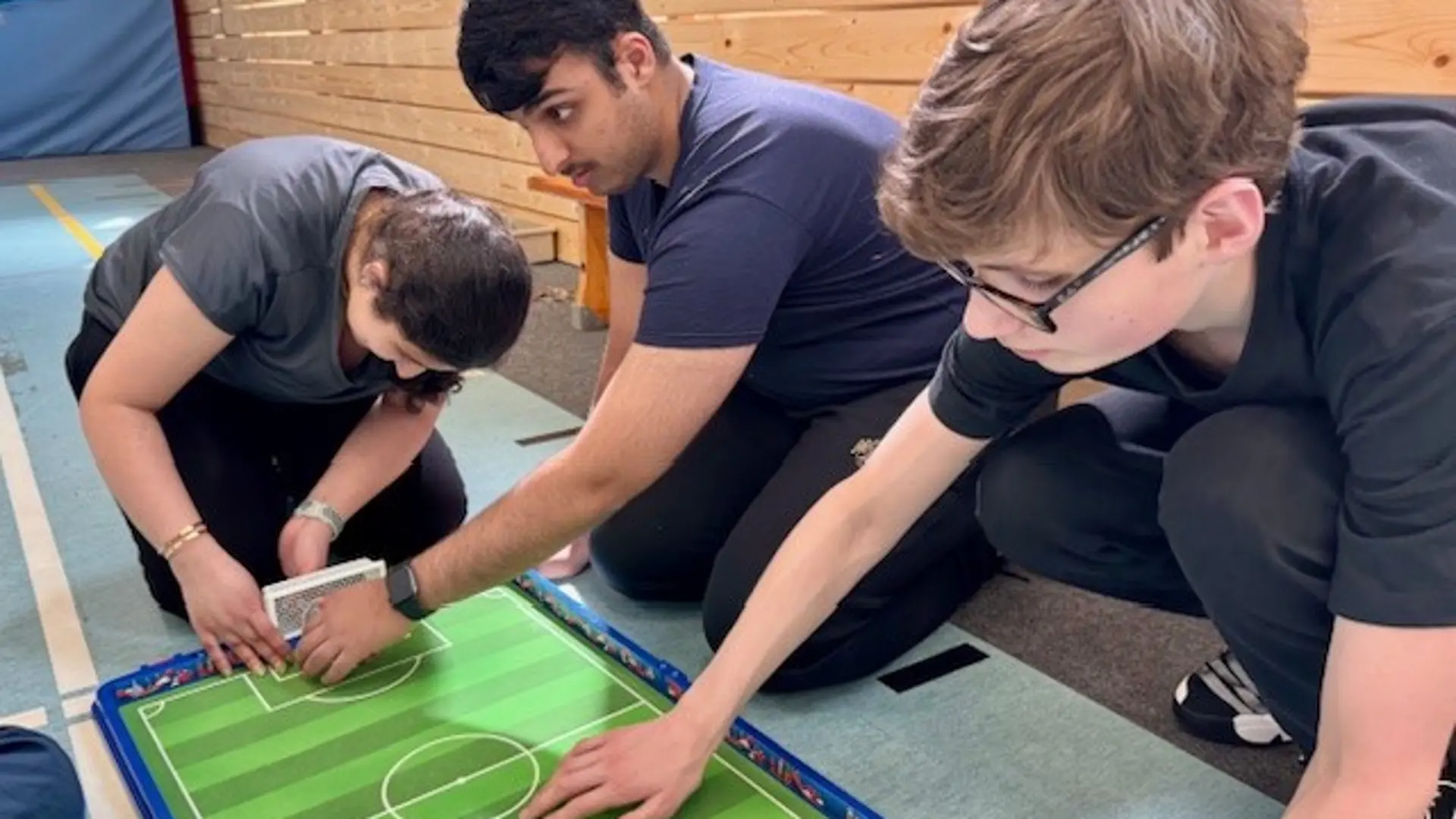 Drei Schüler*innen erkunden ein Modell von einem Fußballplatz