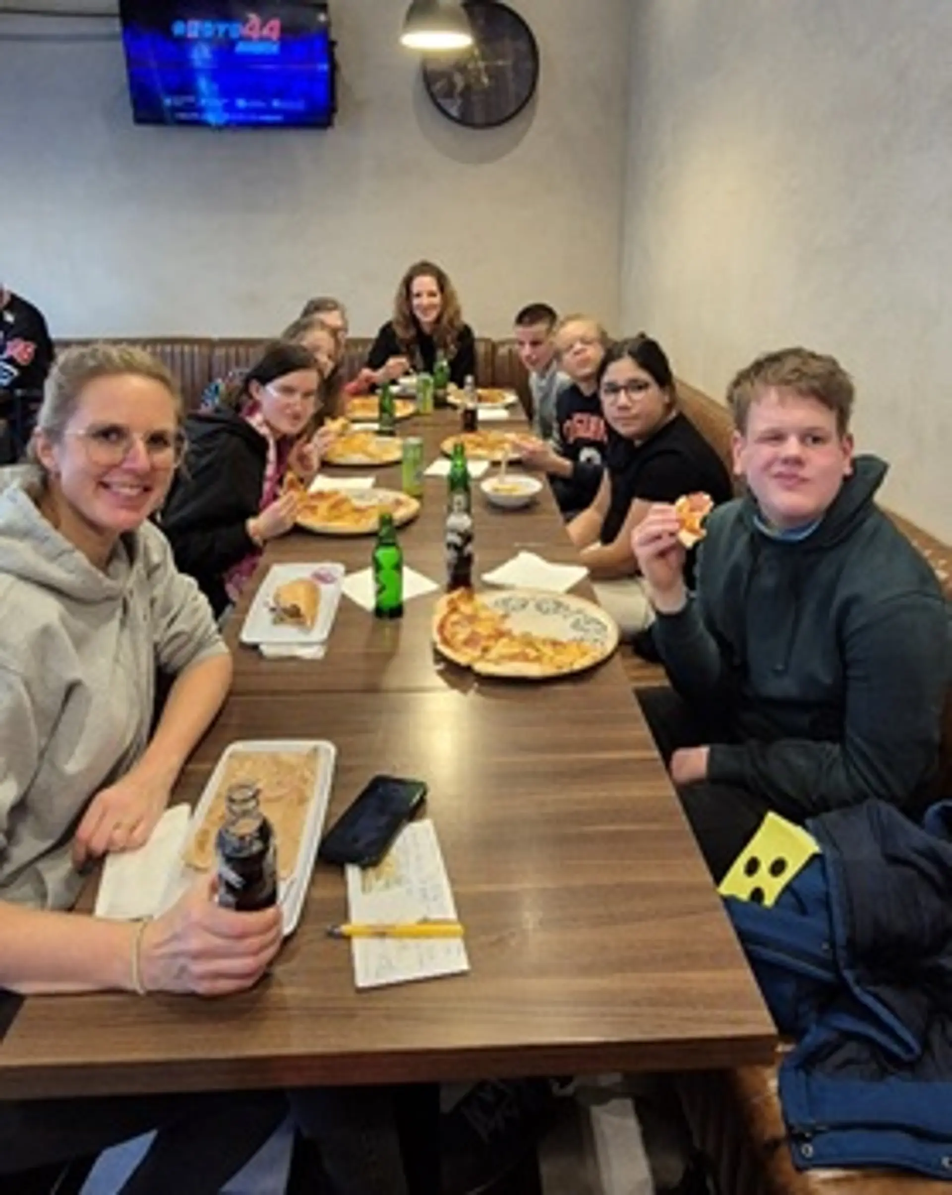 Die gesamte Gruppe sitzt an einem langen Tisch mit Pizza, Döner, Pommes und Getränken.