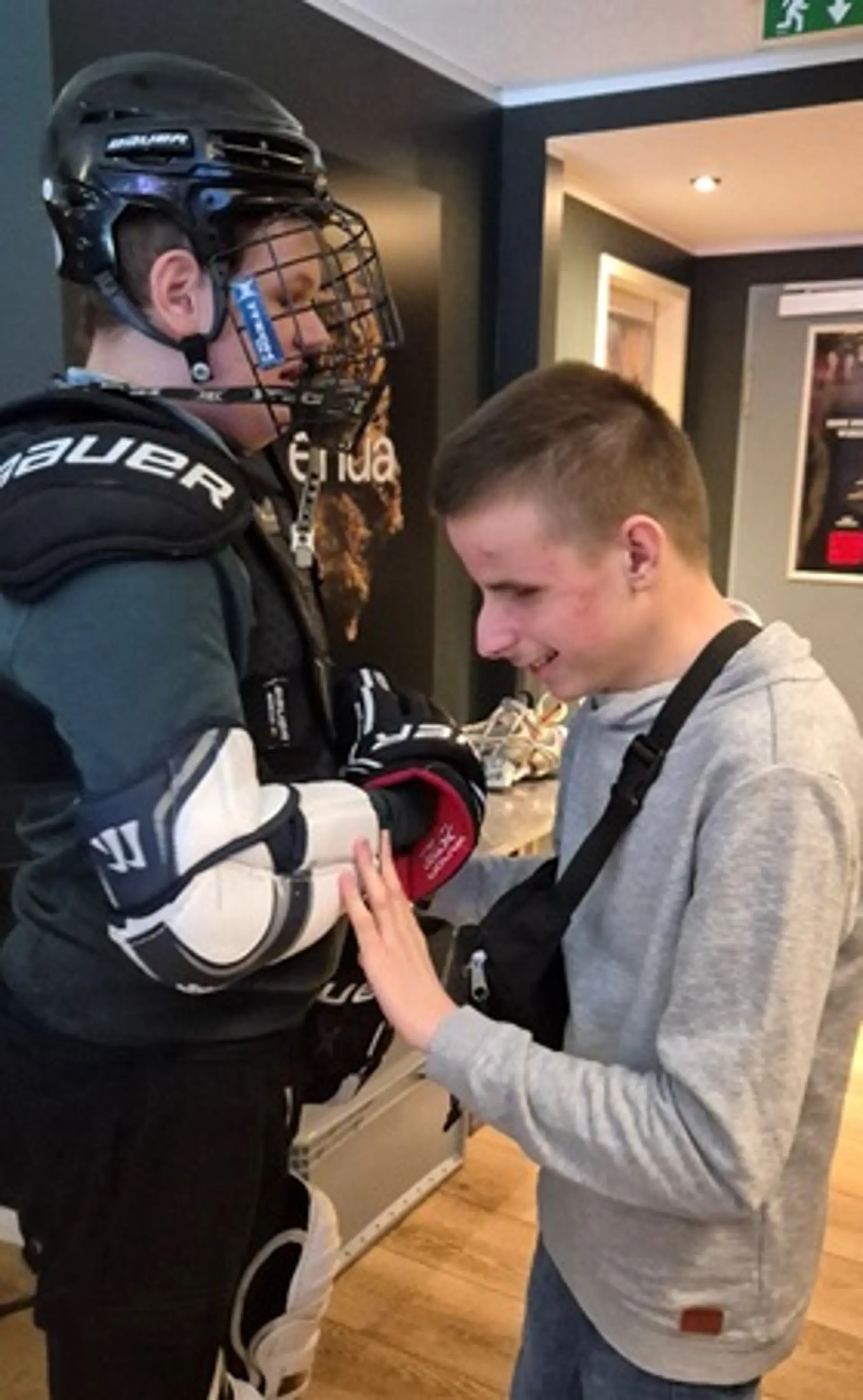 Schüler in voller Eishockeymontur, ein weiterer Schüler ertastet den Armschutz.