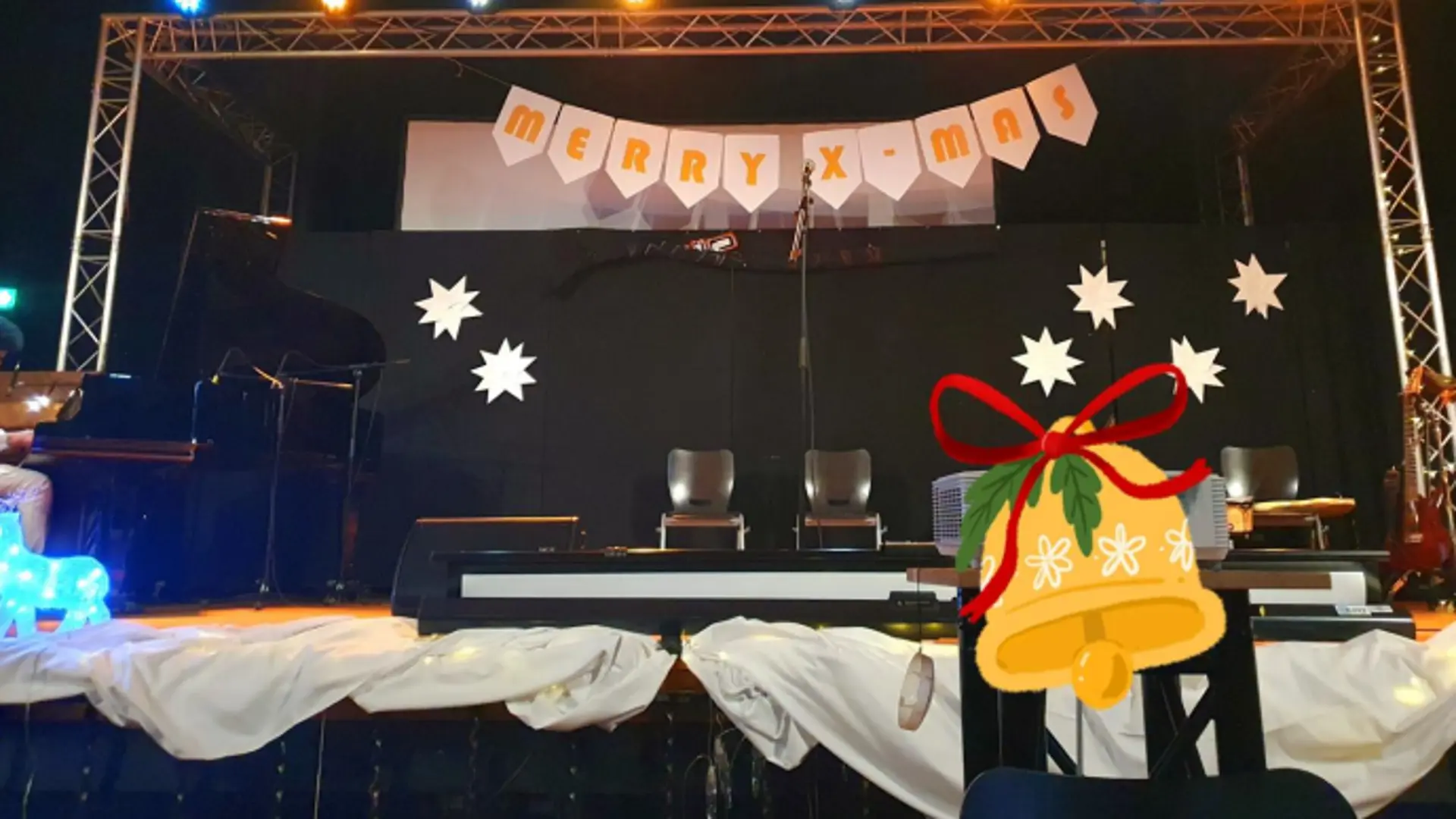 Bild von einer weihnachtlich geschmückten Bühne. Über der Bühne hängt ein Banner mit der Aufschrift "Merry X-Mas"