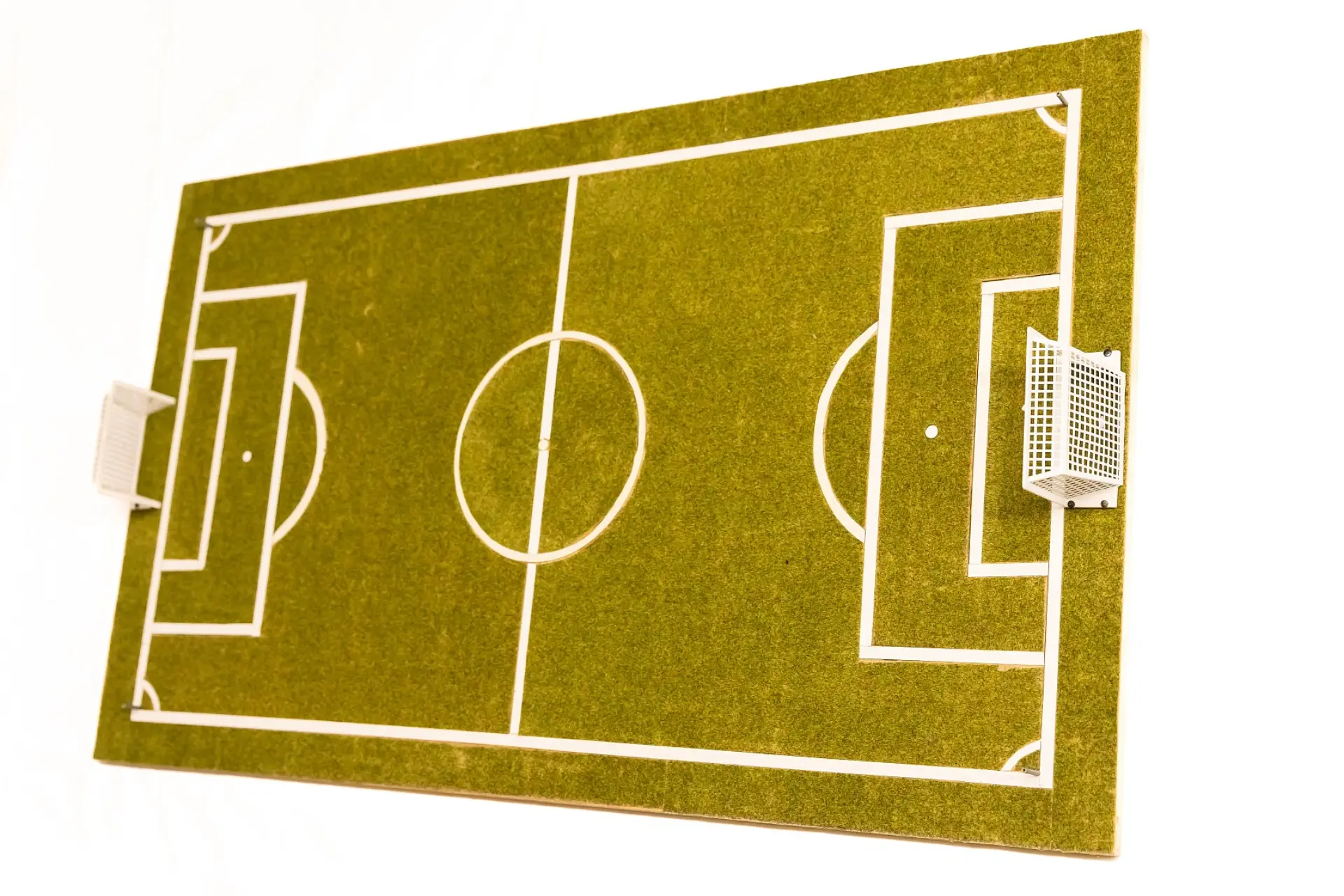 Taktiles Modell von einem viereckigen Fußball-Spielplatz mit Kunstrasen und dicken weißen Linien für die Stadionmarkierungen. In der Mitte von beiden kürzen Seiten befinden sich jeweils ein kleines Netztor aus Plastik.