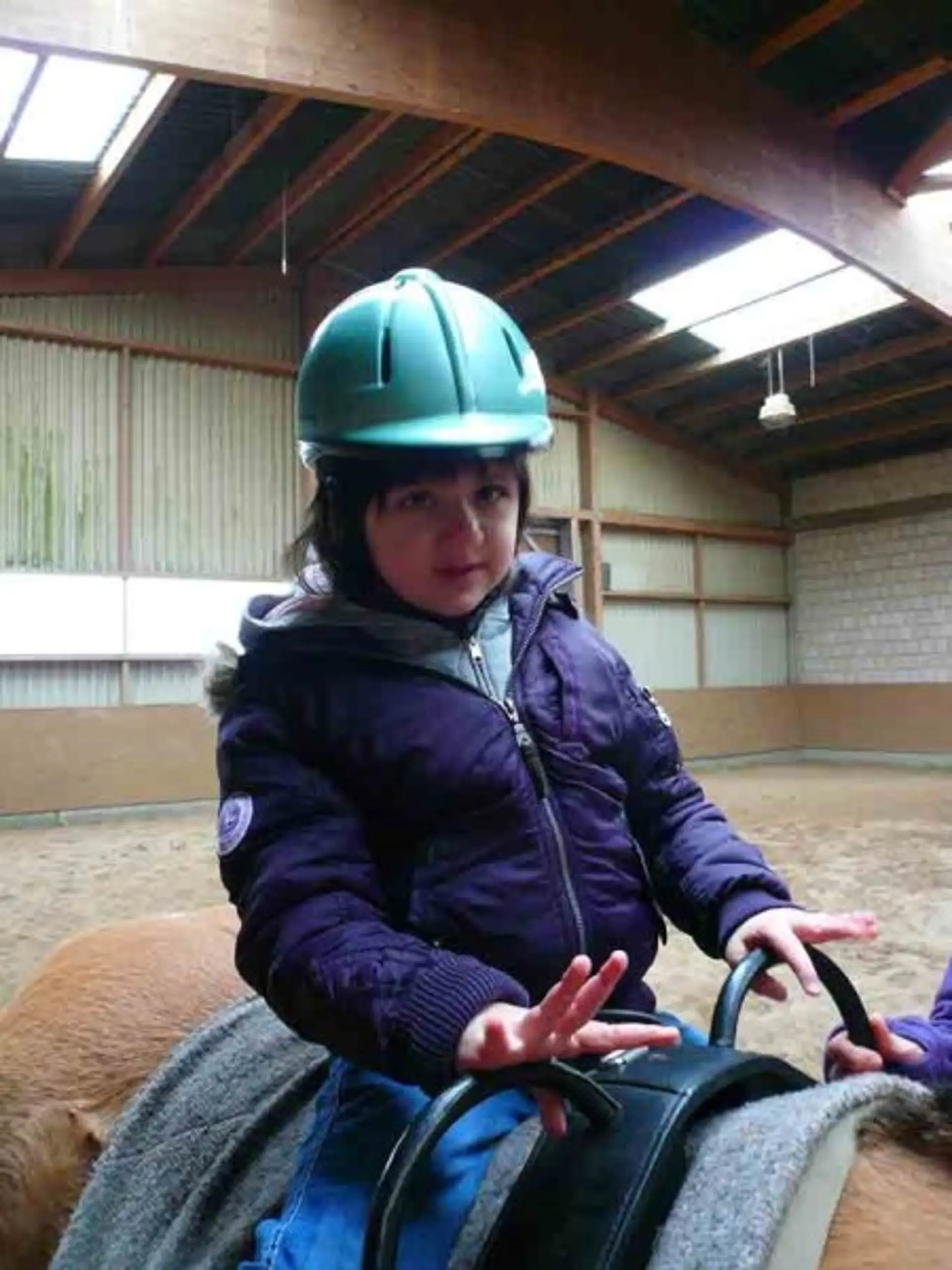 Ein Schulkind mit Schutzhelm sitzt auf einem Pferd und hält sich an der Halterung am Sattel fest.