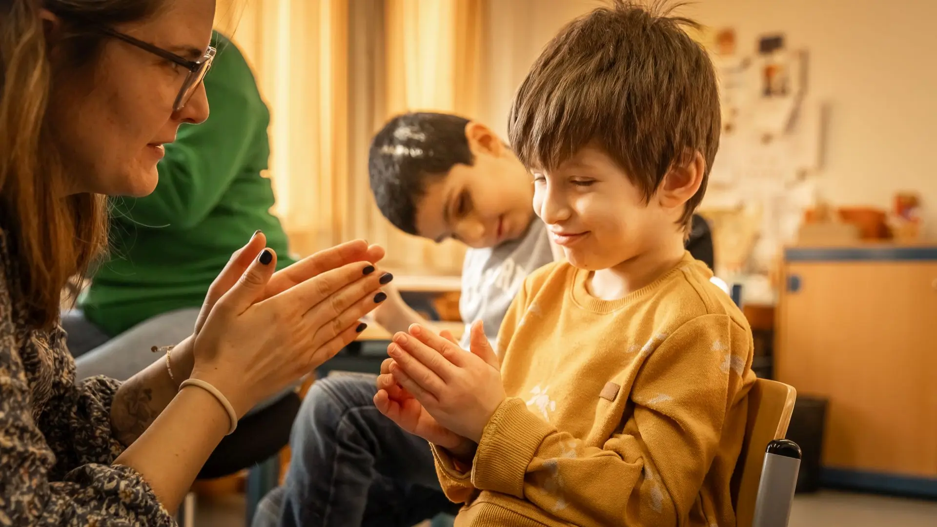 Eine Lehrerin und ein Kind klatschen mit den Händen beim Singen.