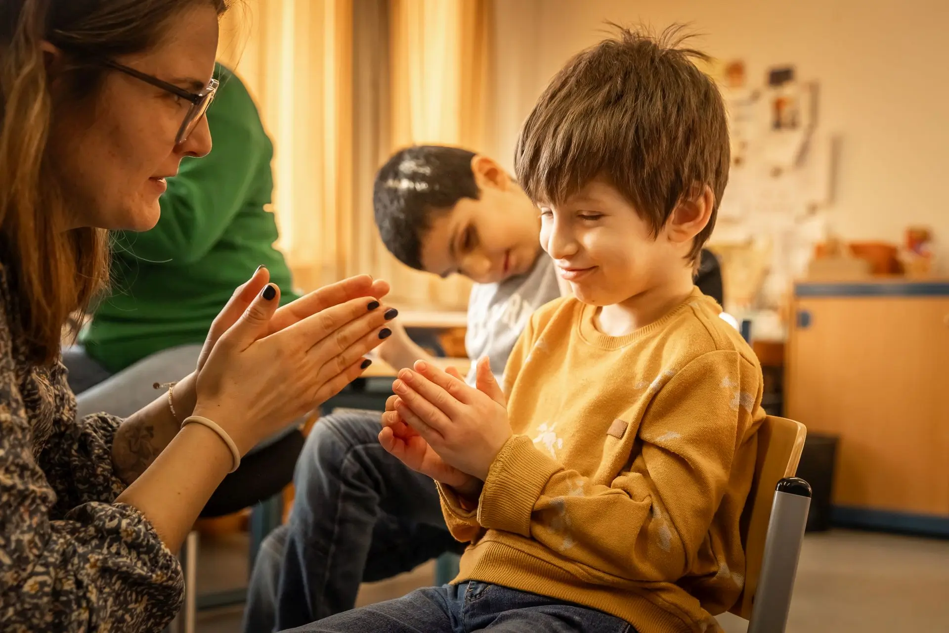 Eine Lehrerin und ein Kind klatschen mit den Händen beim Singen.