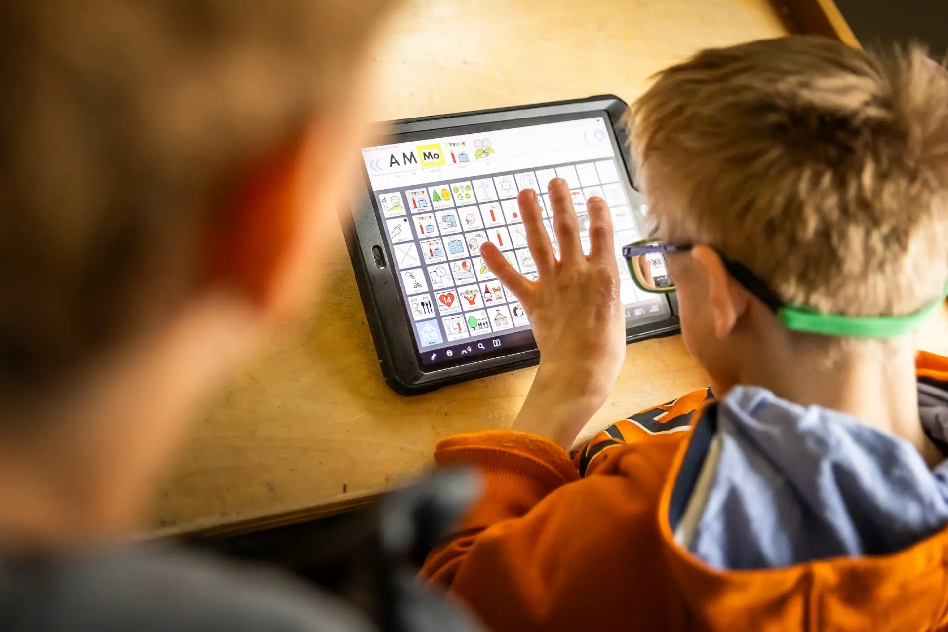 Ein Schüler klickt auf den Metacom-Symbolen auf seinem Tablet, die er zur Kommunikation mit der Lehrkraft neben ihm nutzt.