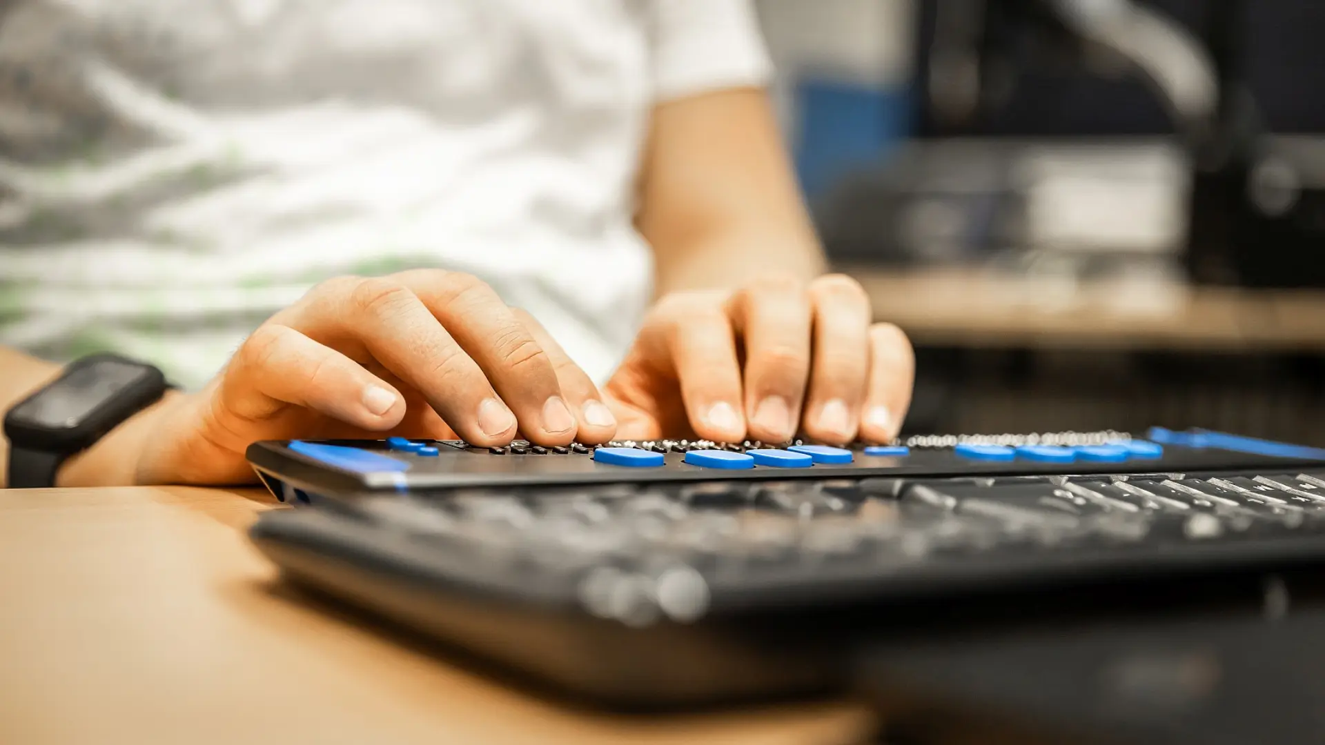 Die Hände eines Schülers, die an einer Tastatur für blinden Menschen tippen. Der Schüler befindet sich in einem Klassenraum