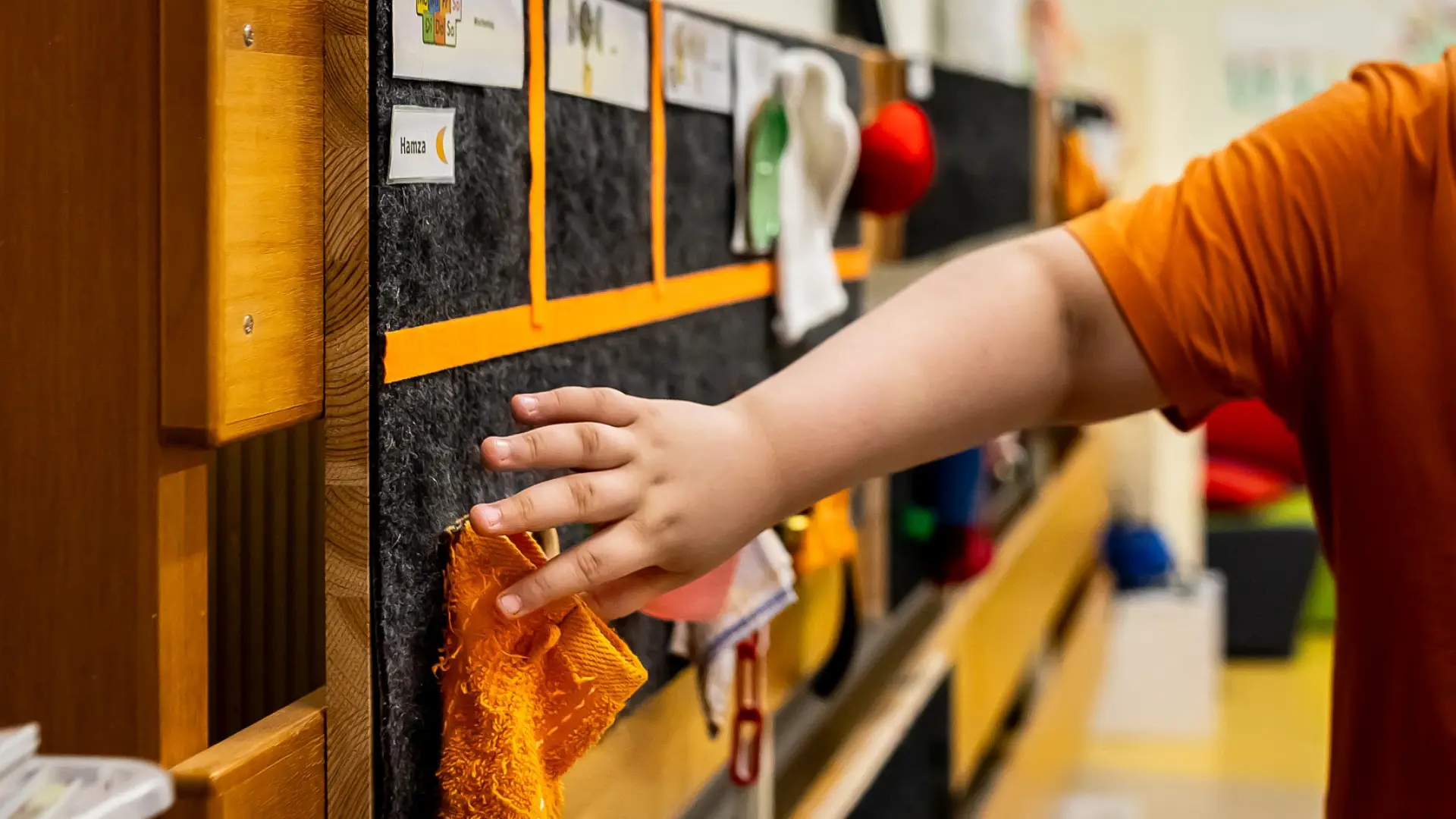 Ein Schulkind geht mit seinen Fingern über einen taktilen Stundenplan. Der Plan ist an der Wand in einem Klassenzimmer angebracht.